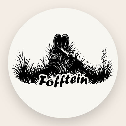 Schwarze Grafik auf Edelstahl: Detailansicht von zwei Gummistiefeln, die entspannt im hohen Gras liegen, darunter der Schriftzug „Fofftein“ in klarer Typografie.