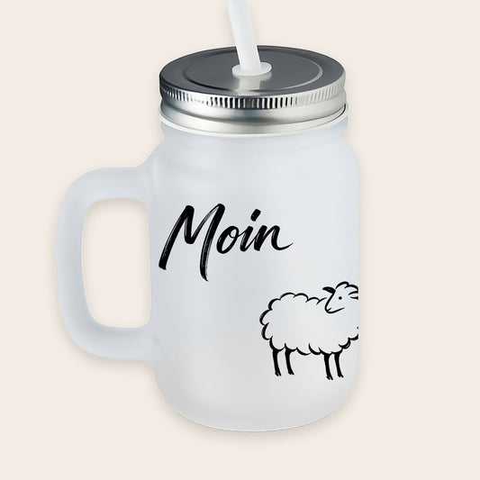 Satiniertes, matt-weißes Trinkglas mit Henkel, Metalldeckel und weißem Strohhalm, bedruckt mit einem schwarzen Schaf-Motiv und dem Schriftzug „Moin“.