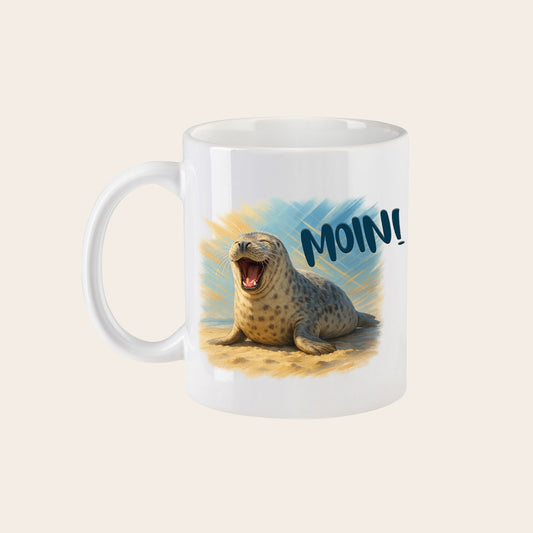 Weißer Keramikbecher mit Henkel, bedruckt mit einer lachenden Robbe und dem Schriftzug Moin.