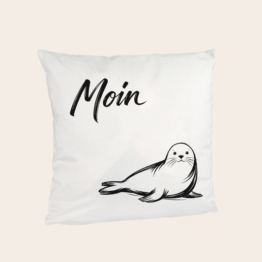 Flauschiges Kuschelkissen mit einer kleinen Robbe und Moin-Schriftzug, ideal für eine nordische Dekoration.